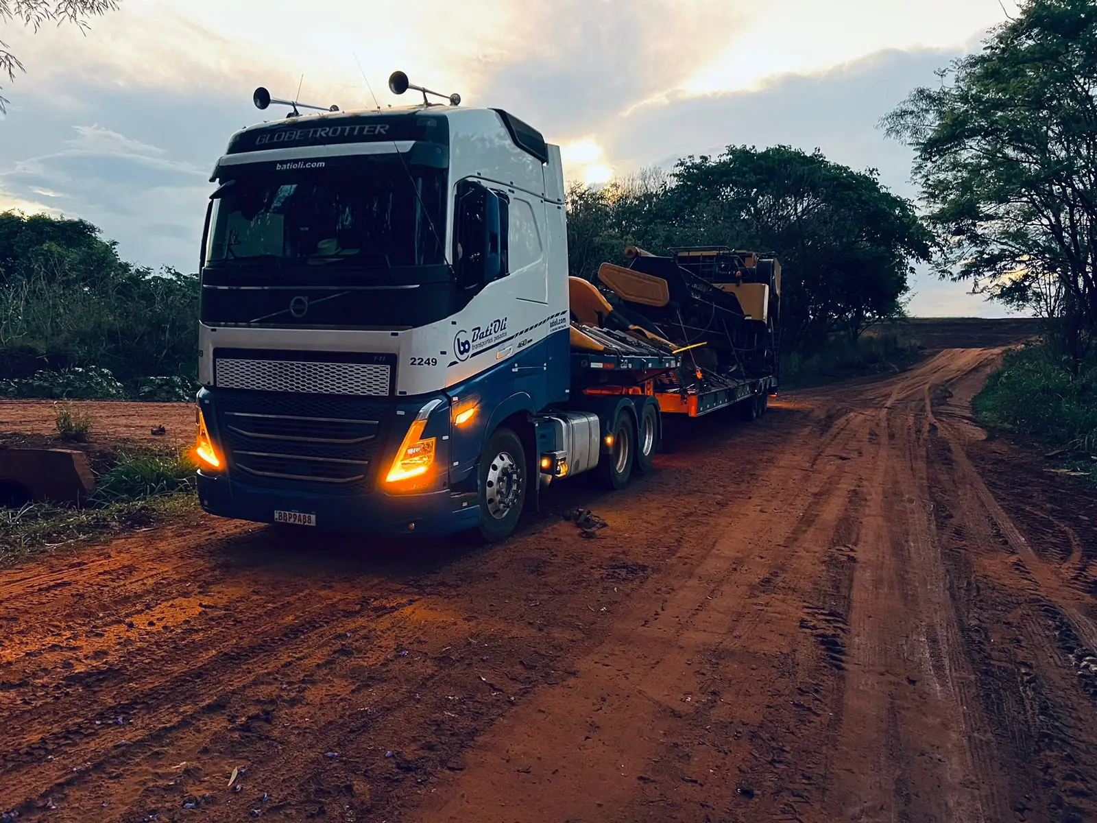 Cavalo mecânico Batioli com prancha carregada em estrada de terra ao entardecer